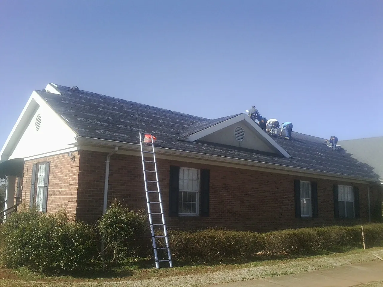 Crew tearing shingles off a brick ranch roof with a ladder set — Metal Roof Repair work by our crew in Niantic