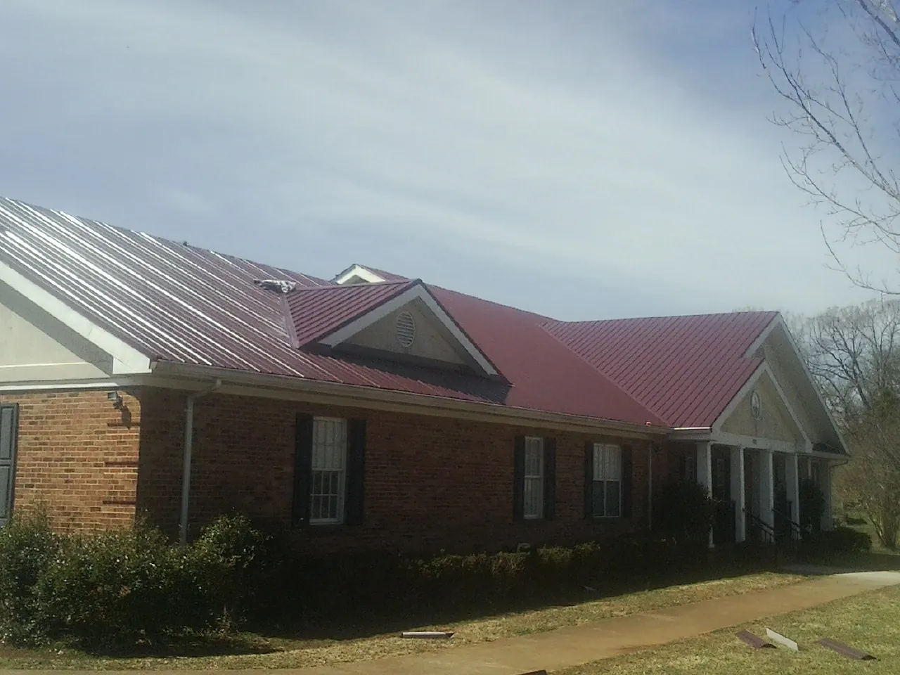 Red metal roof with gabled entries on a long brick building, from a Hail Damage Roof Repair job in Niantic