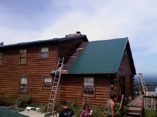Green metal roof going on a two story log home with ladders set in Niantic