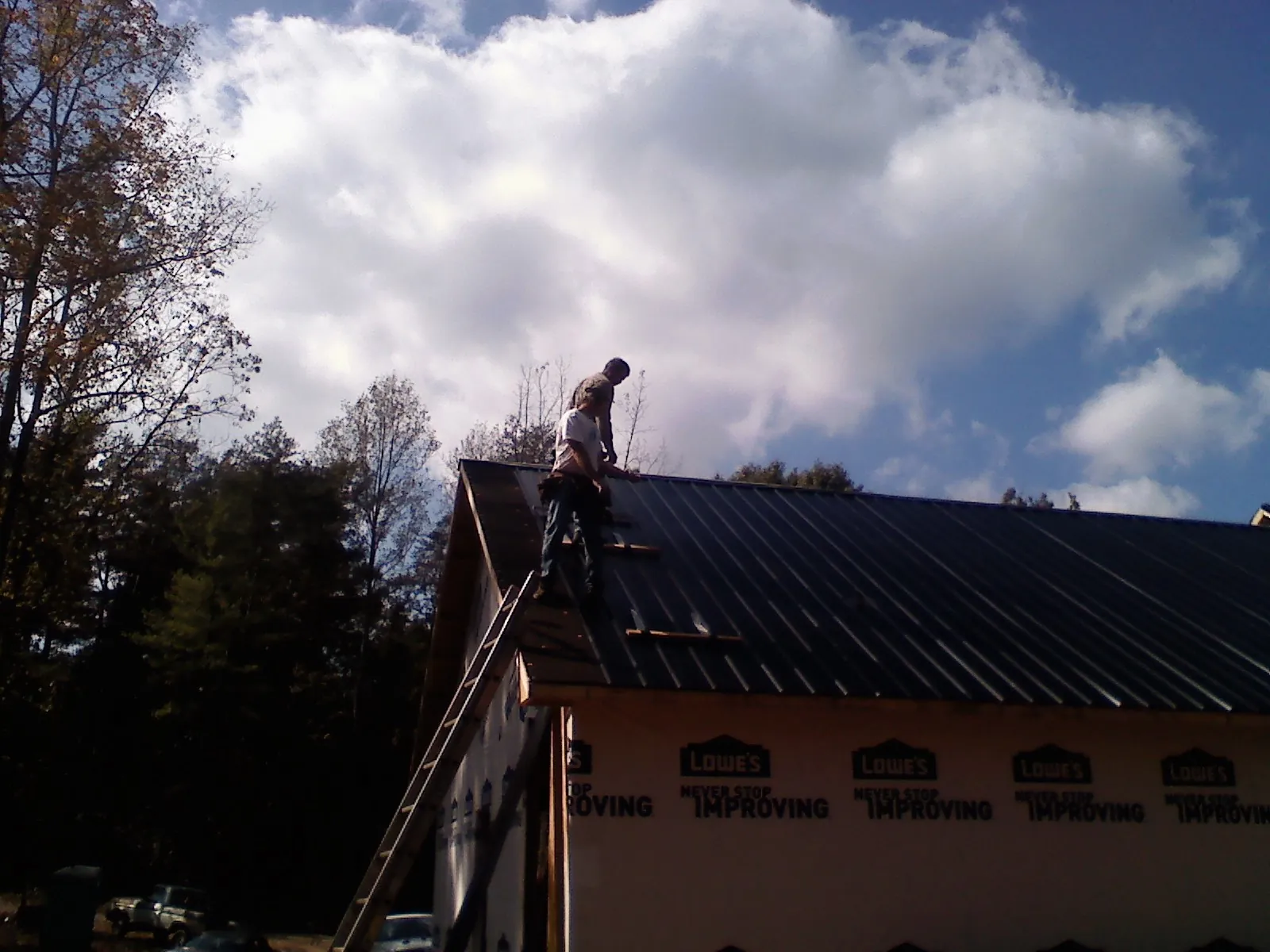 Roofer fastening dark metal panels high against a cloudy sky, from a Roof Inspection job in Niantic