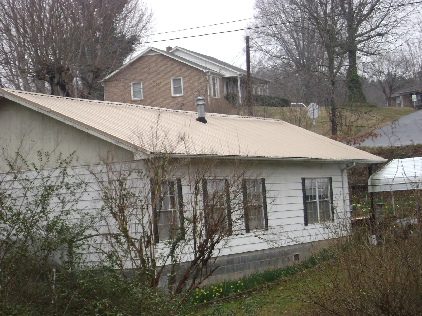 Tan metal roof on a white sided house set into a hillside — Commercial Roofing by Roofing Brothers in Niantic