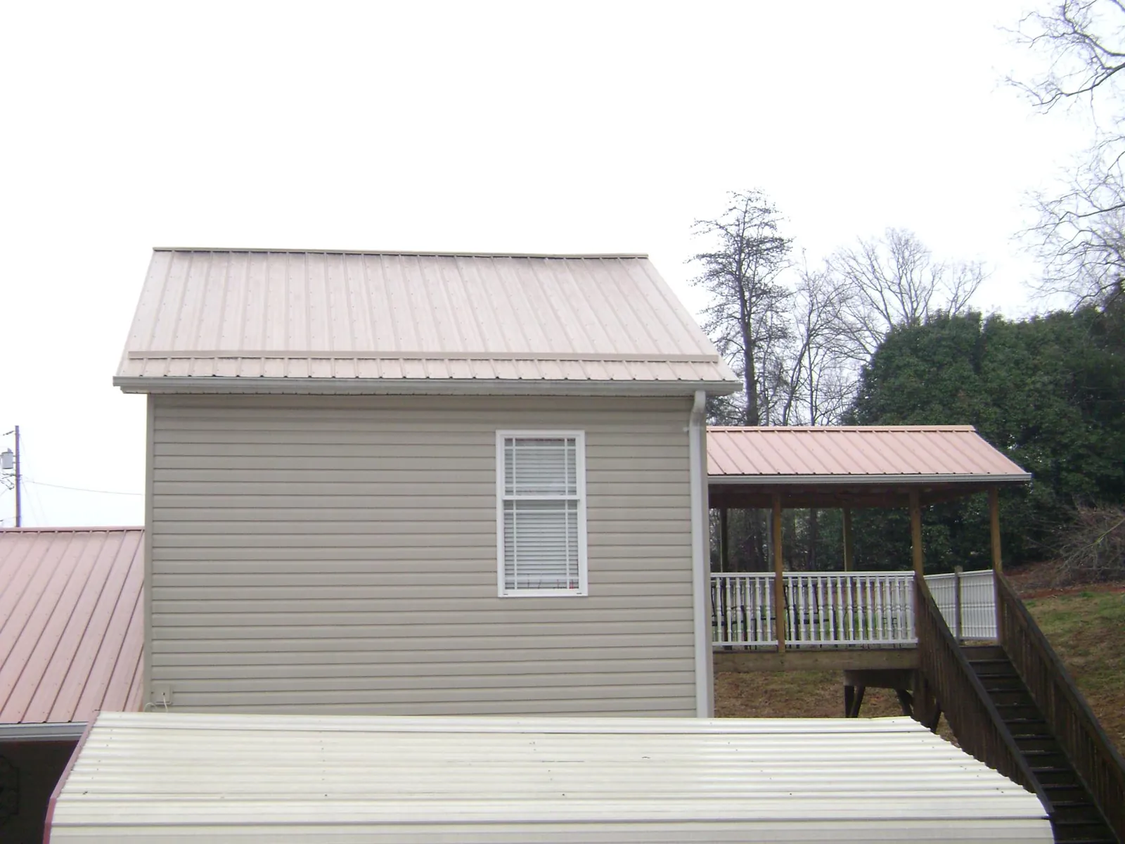 Tan metal roofs on a two story addition and attached porch, from a Roof Replacement job in Niantic